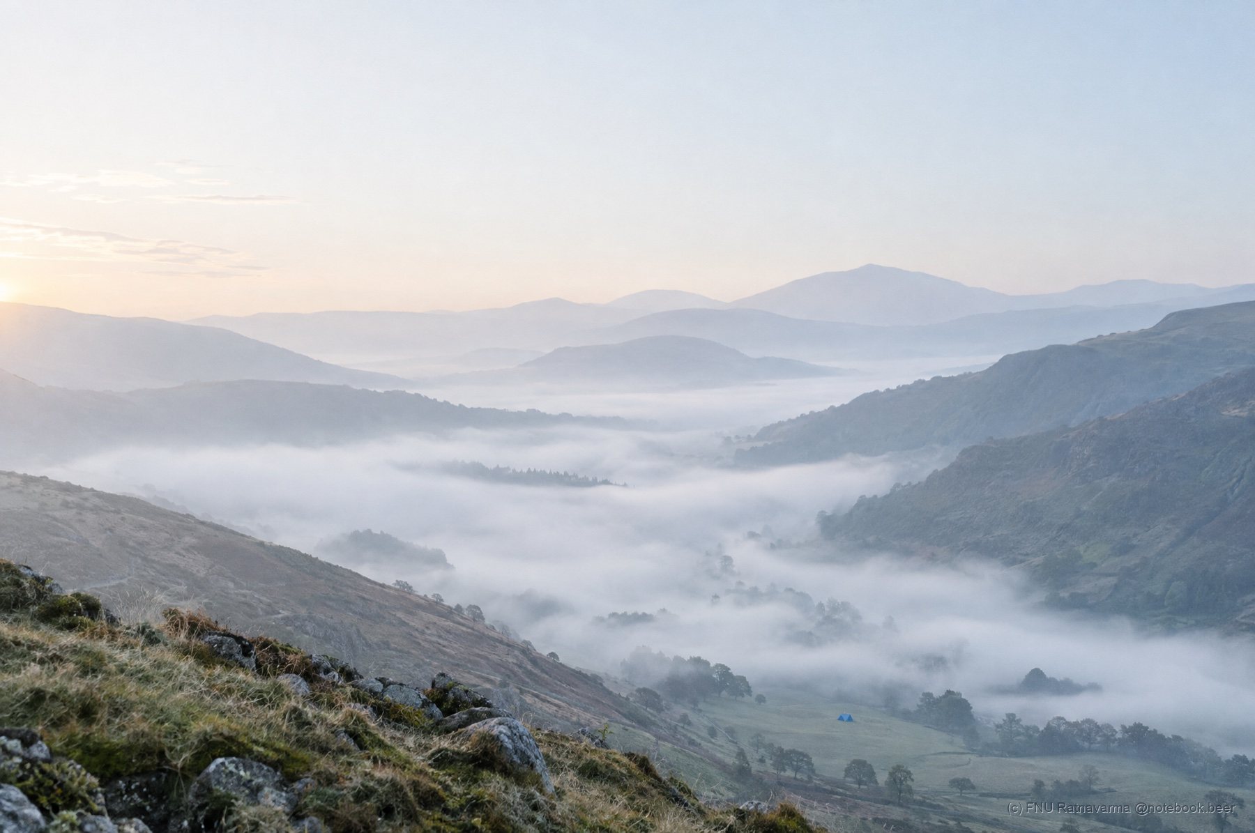 A hidden valley filled with morning mist, ridges fading into the distance under a soft sky.
